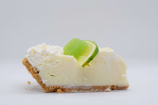 Slice of creamy lime pie topped with whipped cream and lime slice on graham cracker crust.